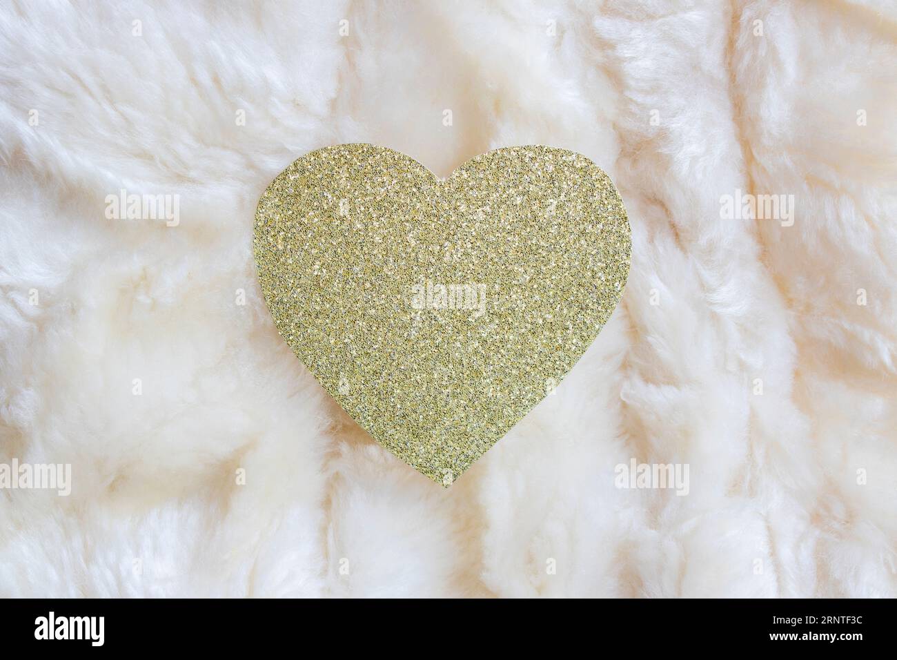 coeur de paillettes dorées sur fond de tapis en fausse peau de mouton. contexte pour les fêtes et les célébrations Banque D'Images