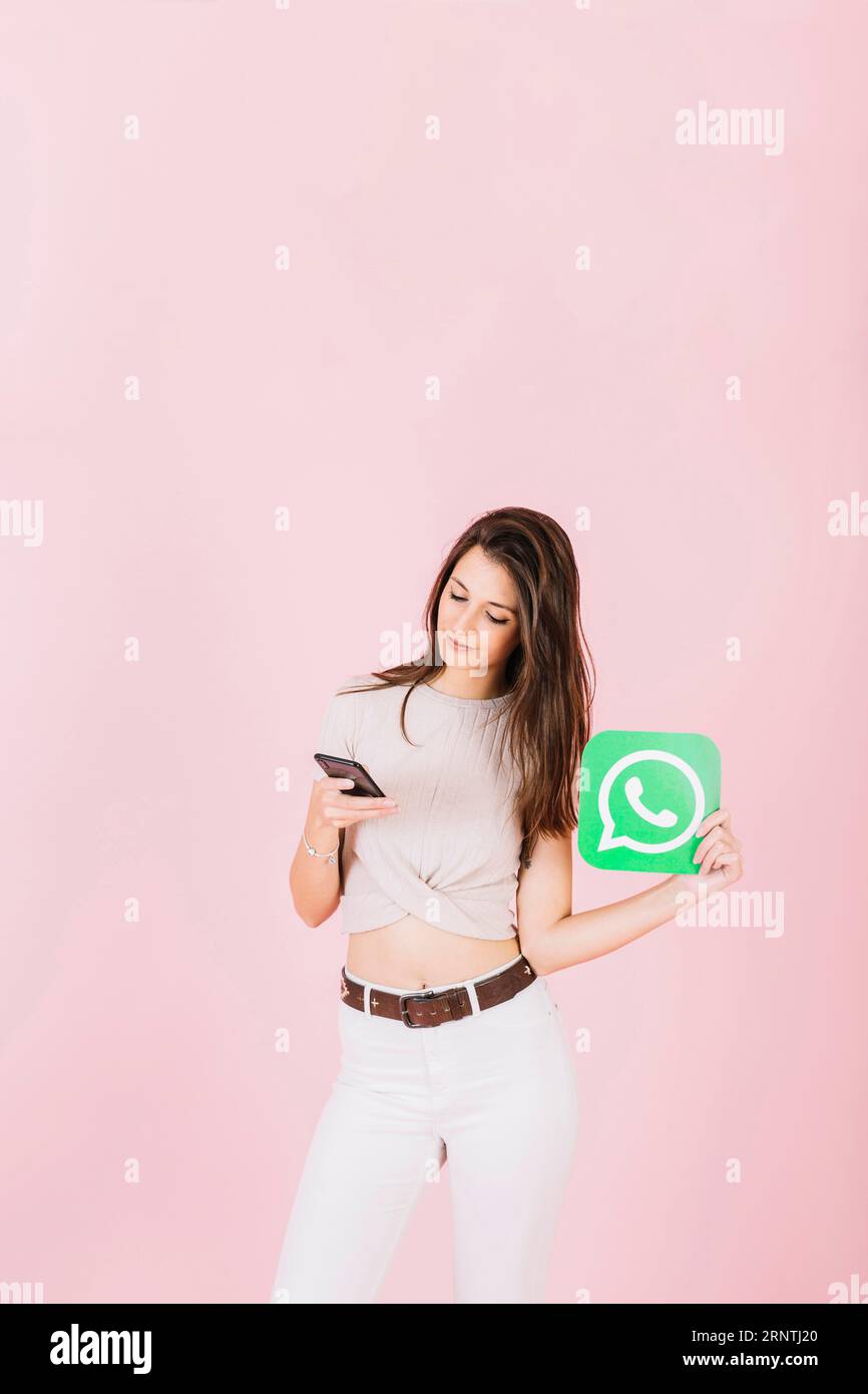 Belle jeune femme tenant l'icône whatsapp à l'aide d'un téléphone portable Banque D'Images