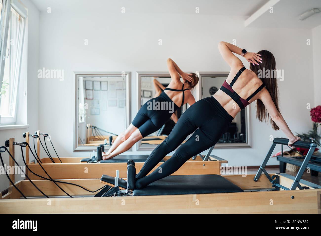 Deux femmes souriantes en forme de coupe faisant des planches latérales avec des muscles du noyau statique de bras levé à l'aide de la machine de reformage Pilates dans la salle de sport athlétique Banque D'Images