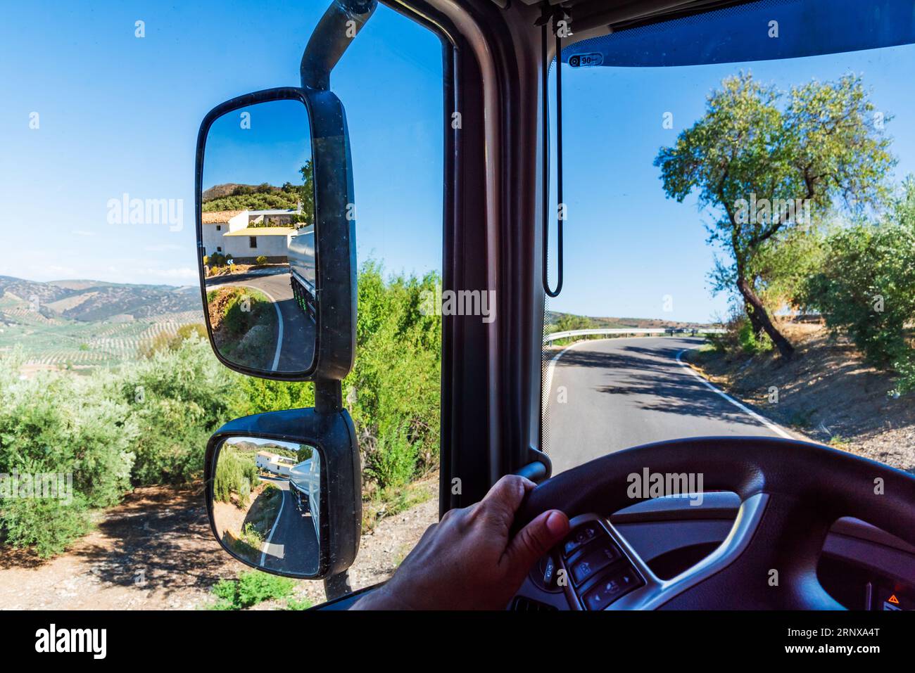 Vue depuis la cabine d'un camion d'une route étroite et le rétroviseur où vous pouvez voir le virage serré de la remorque-citerne. Banque D'Images