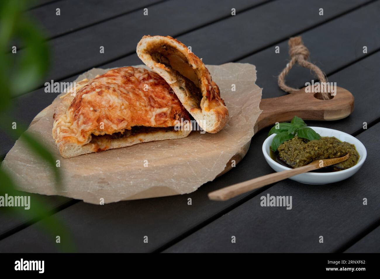 Pizza calzone découpée avec sauce tomate, pesto vert et fromage sur assiette en bois Banque D'Images