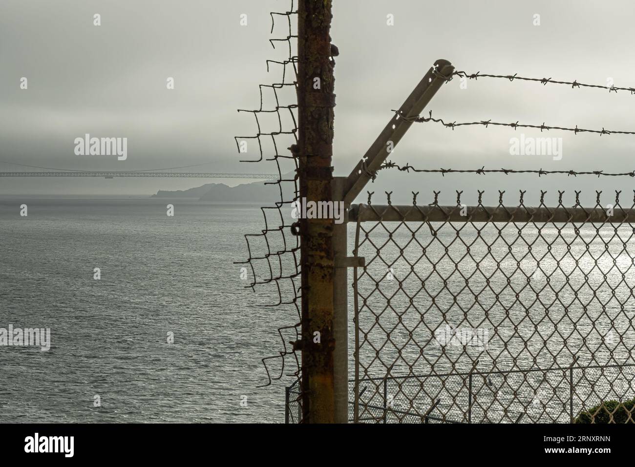 San Francisco, CA, USA - 12 juillet 2023 : à l'intérieur de la prison historique d'Alcatraz. Pont du Golden Gate sous un ciel brumeux de fin de journée derrière des barbelés Banque D'Images