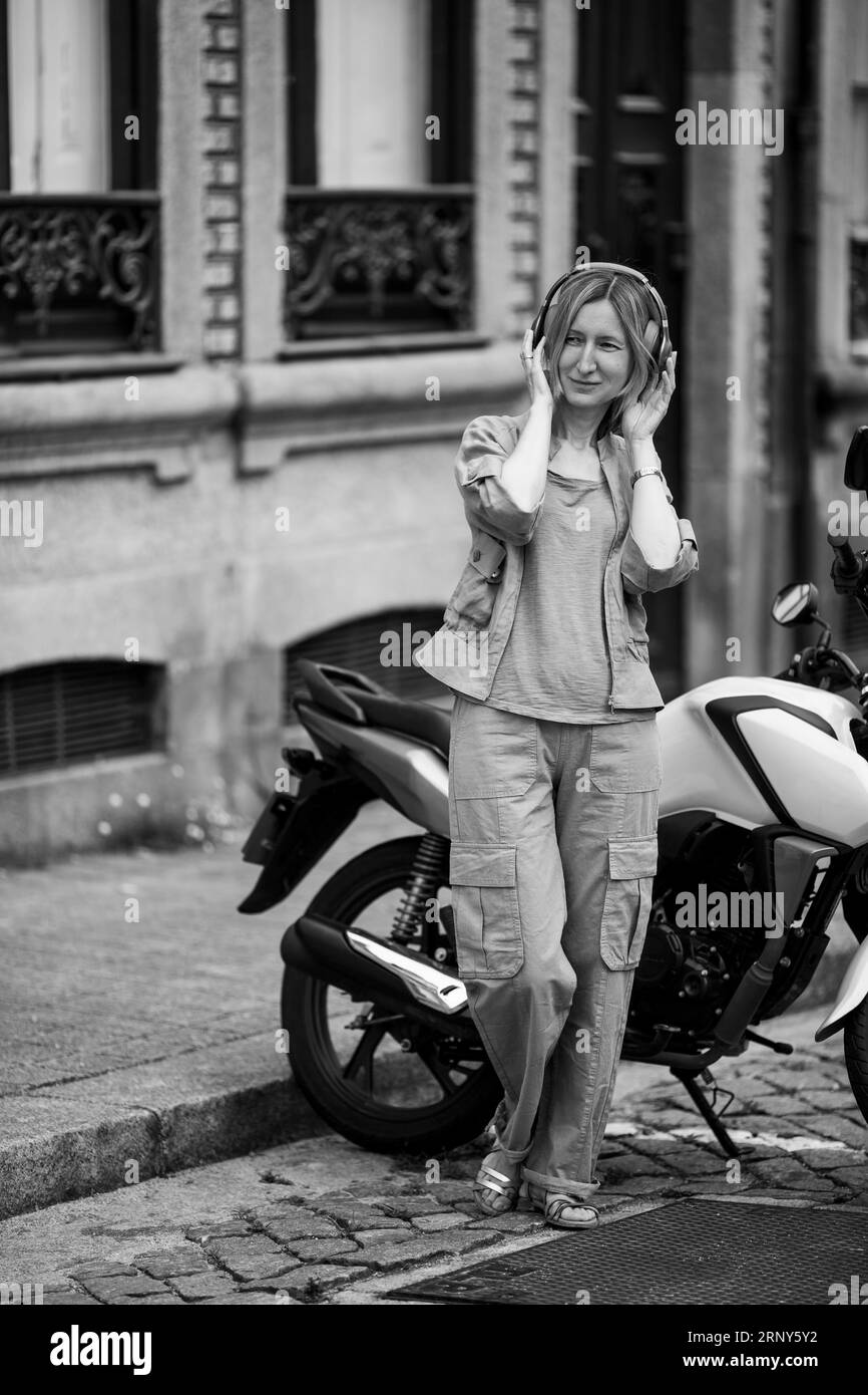 Femme avec des écouteurs debout dans la rue près de la moto. Photo noir et blanc. Banque D'Images