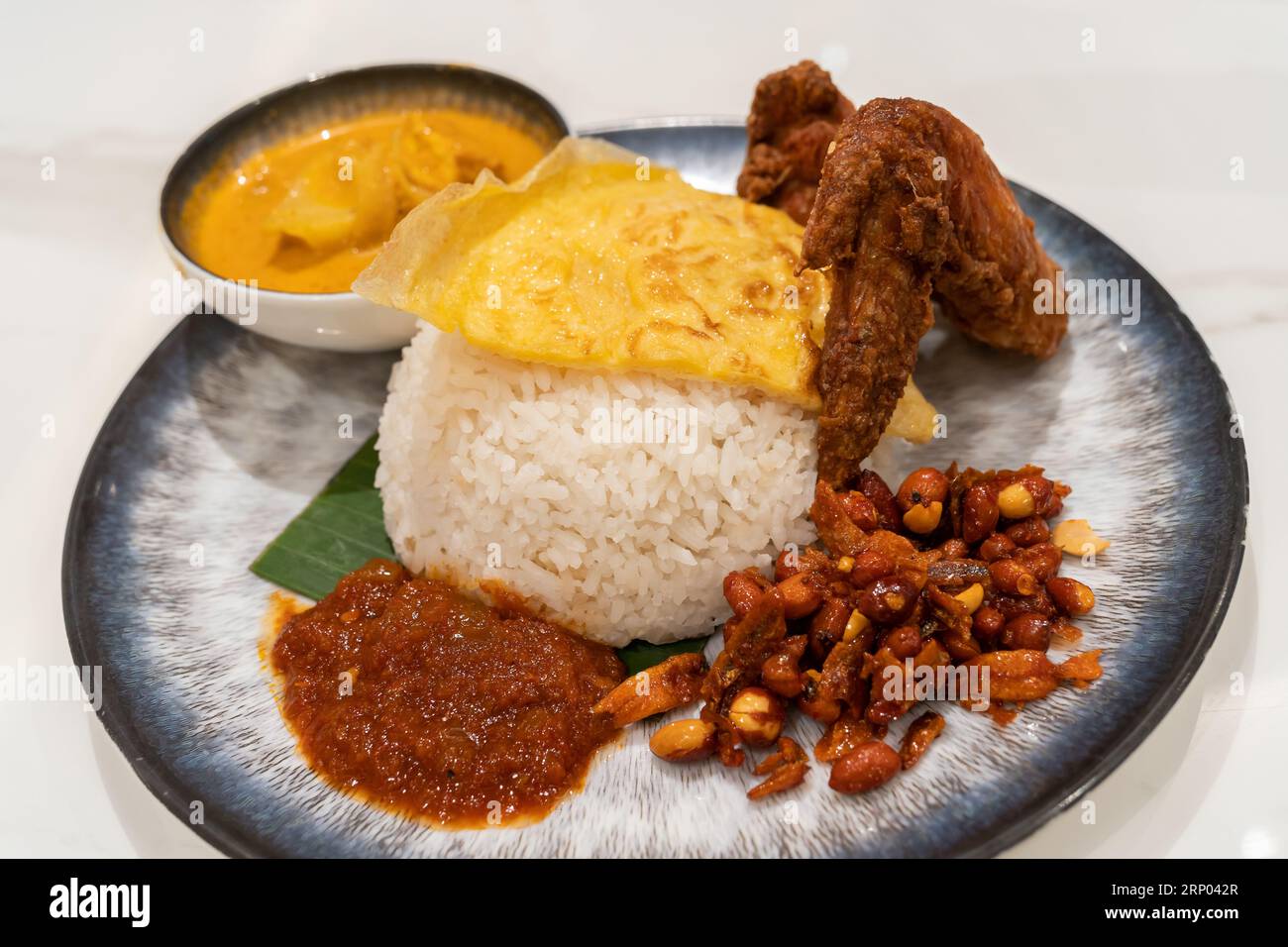 Cuisine asiatique Nasi Lemak est un plat de riz infusé avec du lait de coco. Servi avec sambal, aile de poulet frite, cacahuète frite, œuf frit avec sauce au curry. Banque D'Images