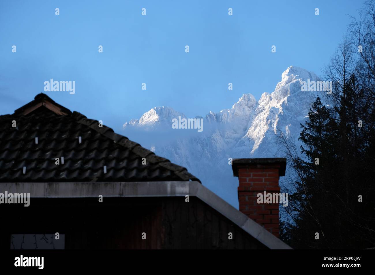 Les sommets enneigés des Alpes juliennes s'élèvent au-dessus d'un toit à Kransjka Gora, en Slovénie. Banque D'Images
