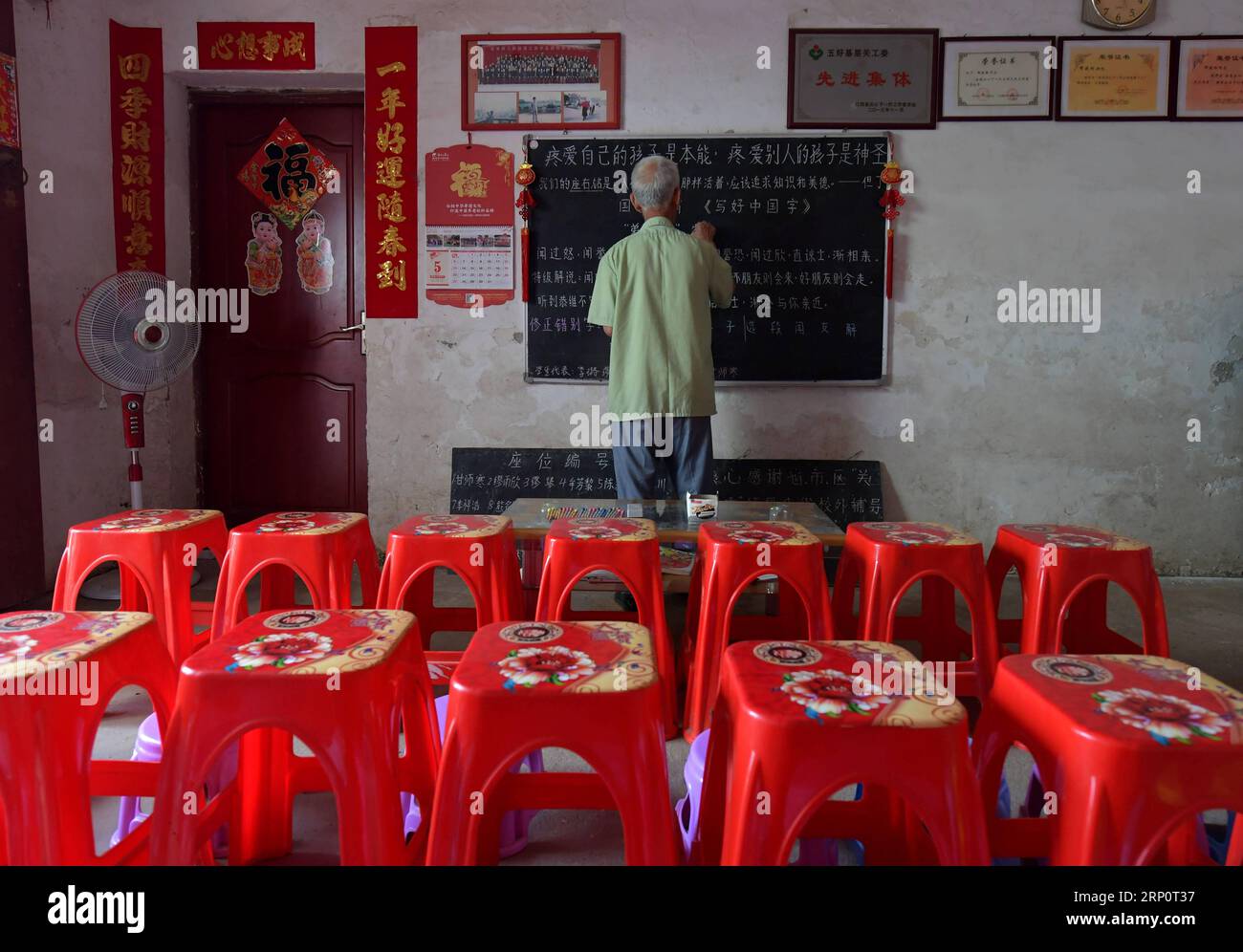 (180524) -- NANCHANG, 24 mai 2018 -- Miao Yanxiang écrit de vieux dictons sur le tableau noir du poste de garde pour enfants laissés derrière lui à son domicile de la ville de Shibu, ville de Nanchang dans la province de Jiangxi dans l'est de la Chine, le 23 mai 2018. Miao, âgé de plus de 70 ans, a créé un poste de garde pour les enfants laissés derrière lui dans sa propre maison en 2009, où il a fourni une place gratuite pour les enfants pour faire leurs devoirs et étudier après l'école. Ayant reçu plus de 3 000 enfants au cours des neuf dernières années, Miao est satisfait de son travail bénévole et voit les progrès des enfants. (ZWX) CHINA-JIANGXI-LEFT-BEHIND ENFANTS-ELDER C. Banque D'Images