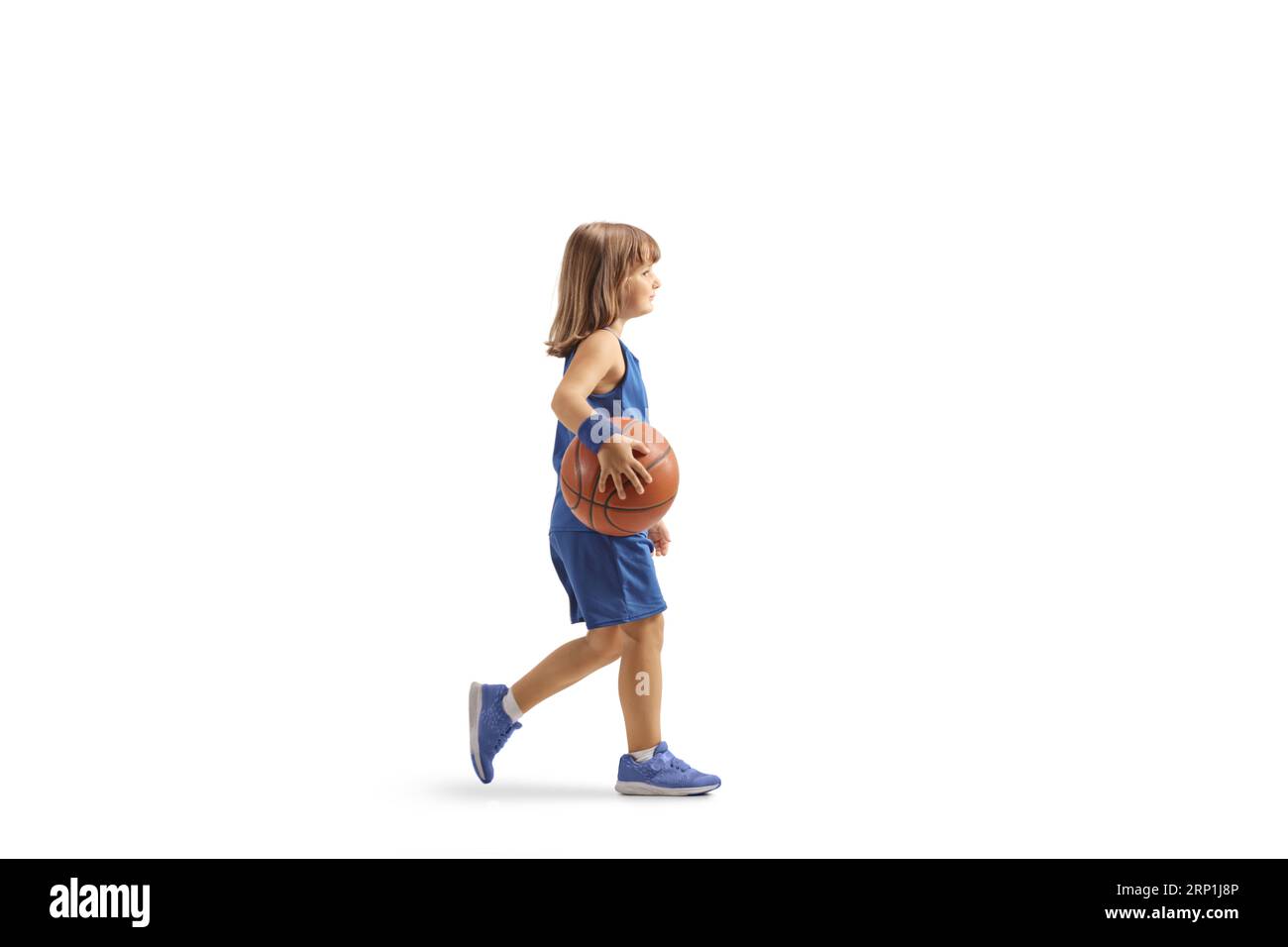 Petite fille dans un maillot bleu de basket-ball marchant et tenant une balle isolée sur fond blanc Banque D'Images