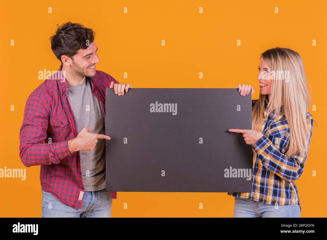Portrait jeune couple pointant leur doigt blanc pancarte noire sur fond orange Banque D'Images