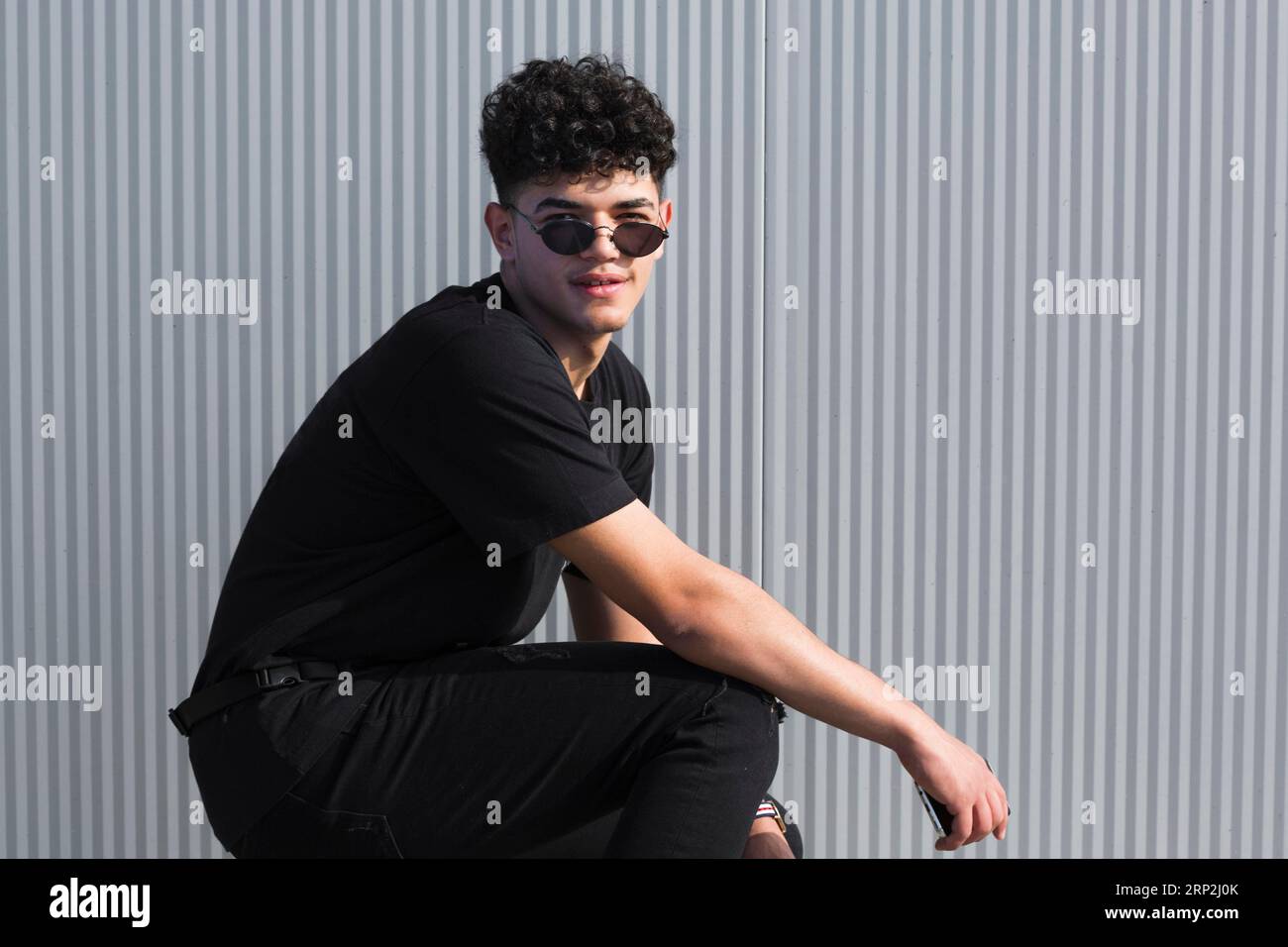 Jeune homme ethnique curly lunettes de soleil vêtements noirs contre le mur gris Banque D'Images