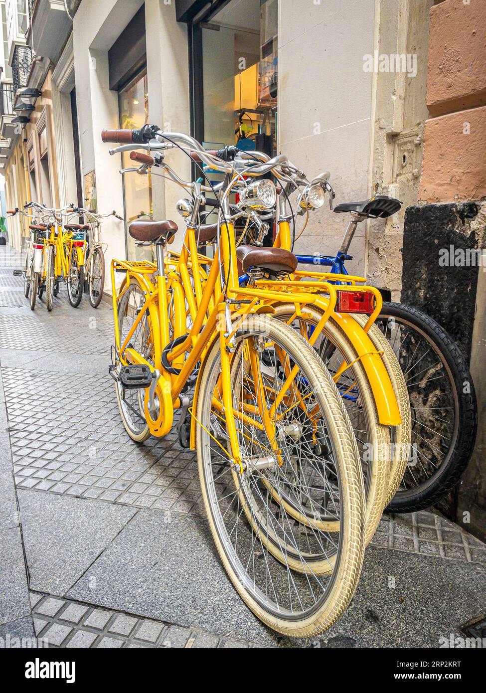Groupe de vélos jaunes à louer devant un magasin de location de vélos sur une rue européenne. Banque D'Images