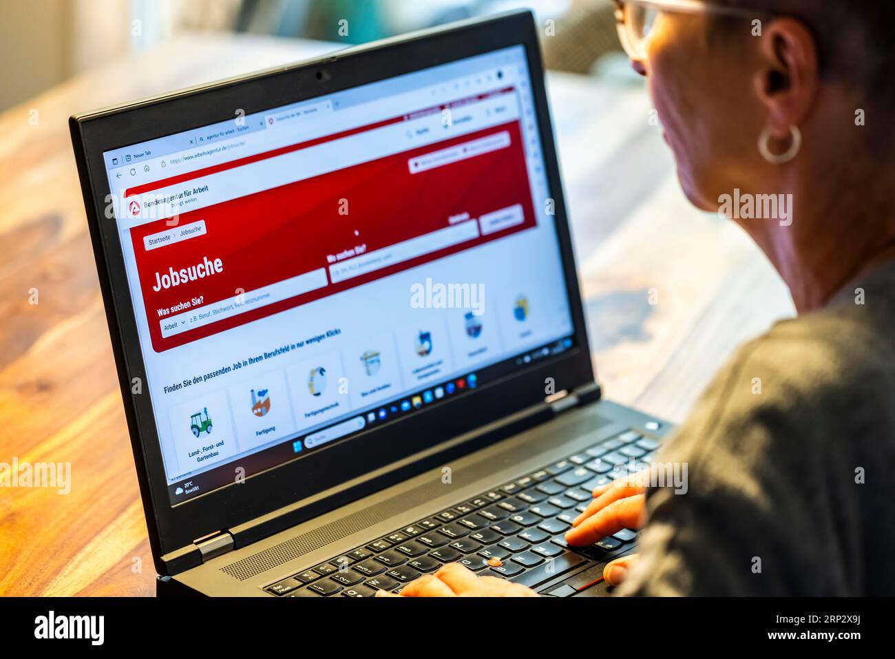 Femme avec des lunettes à la recherche d'un emploi s'assoit à la maison devant son cahier et vérifie le site Internet de l'Agence fédérale pour l'emploi pour le travail Banque D'Images