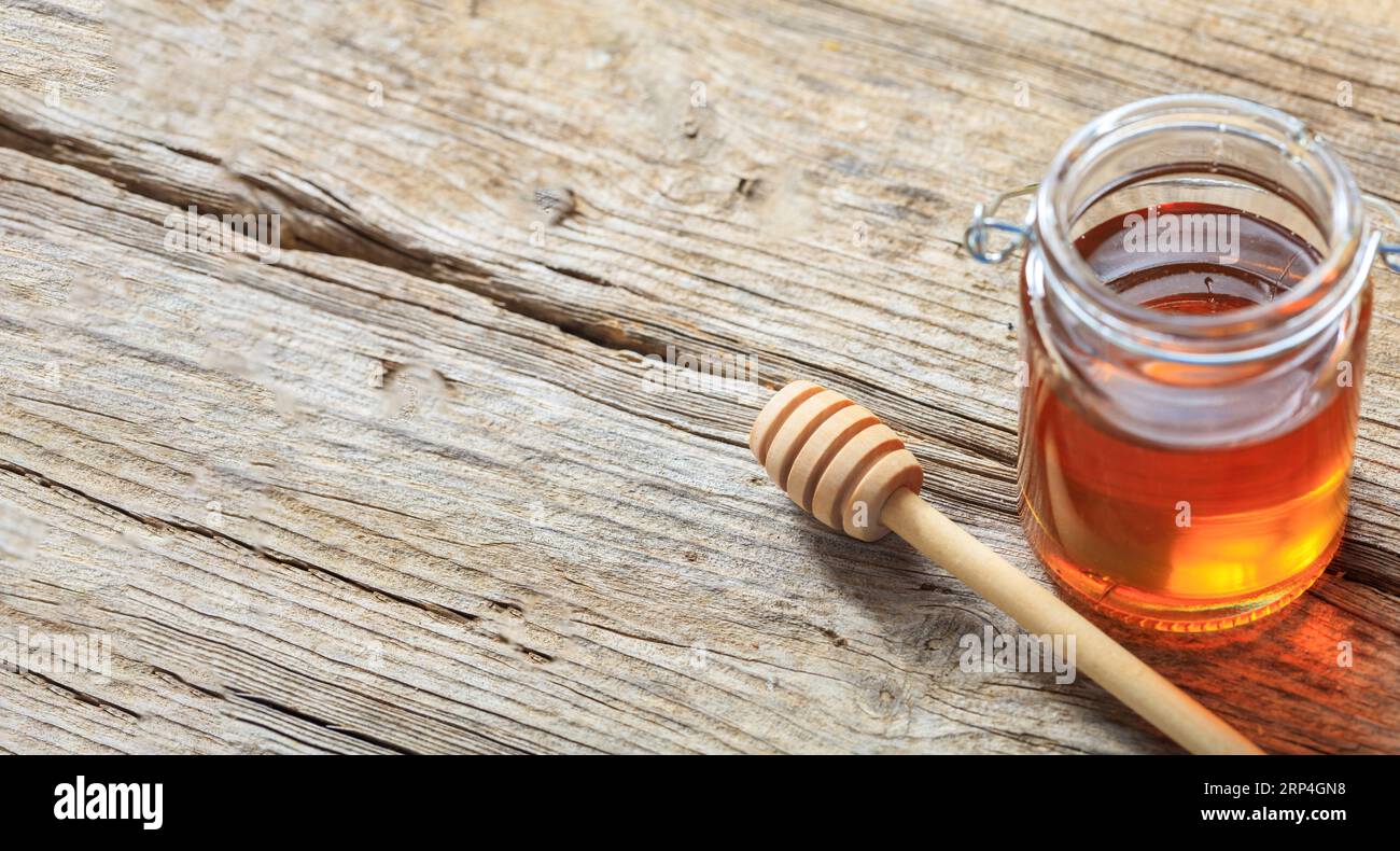 Un pot en verre avec du miel et un bâton sur fond de table en bois. Bol transparent avec produit nutritionnel de couleur or. Vue au-dessus, espace de copie Banque D'Images