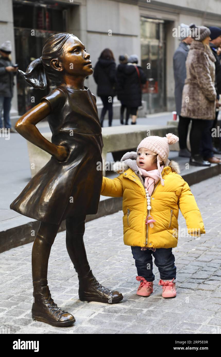 (181210) -- NEW YORK, 10 décembre 2018 -- Une fille regarde la fille sans peur dans la rue devant la Bourse de New York, aux États-Unis, le 10 décembre 2018. Fearless Girl, une célèbre statue en bronze située dans le quartier financier de New York, a été dévoilée lundi matin dans sa nouvelle maison devant la Bourse de New York (NYSE). Fearless Girl a d'abord été installée face à face avec l'emblématique statue de Charging Bull au Bowling Green Park dans le Lower Manhattan, à quelques pâtés de maisons de son emplacement actuel, à la veille de la Journée internationale de la femme en mars 2017 comme temporaire Banque D'Images