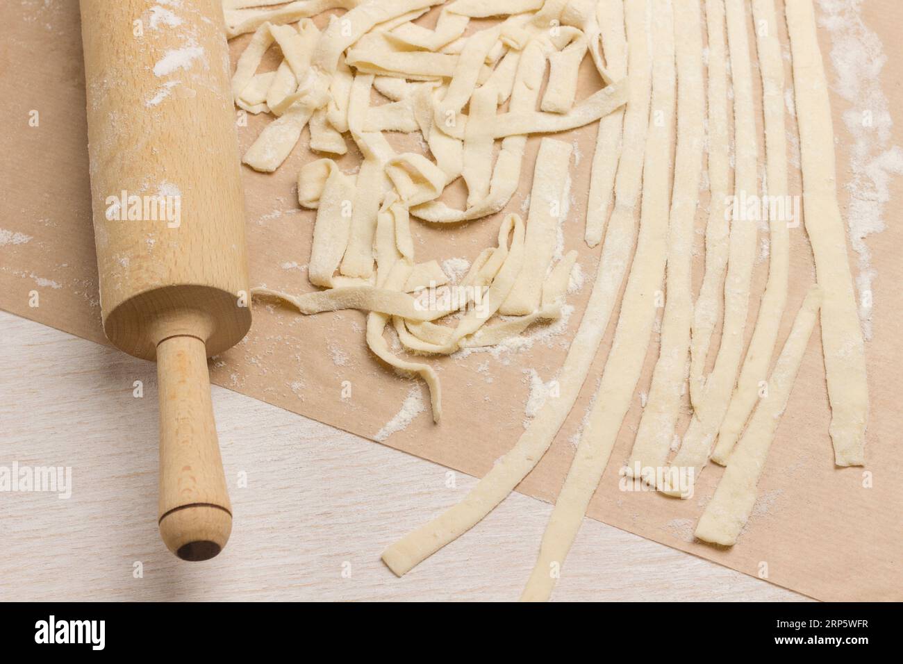 Rouleau à pâtisserie et pâte coupés en lanières. Le processus de fabrication de nouilles maison. Fond en bois Banque D'Images