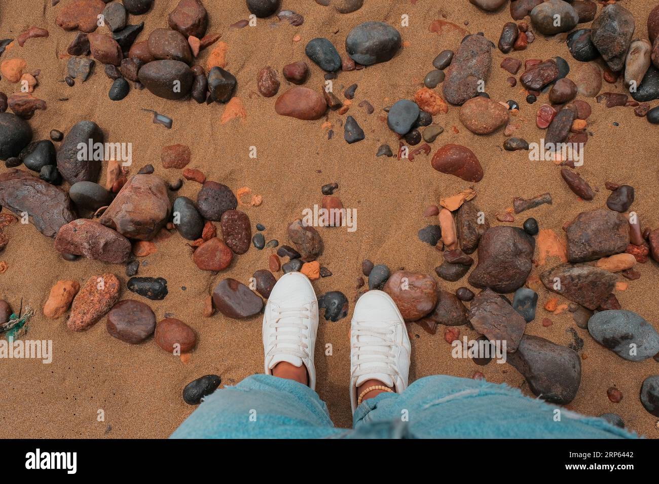 En regardant vers le bas le sable et les rochers à Legzira Beach. Littoral accidenté dans la province de Tiznit au Maroc, Afrique. Prise de vue en perspective. Jeans bleus, chaussures blanches. Banque D'Images