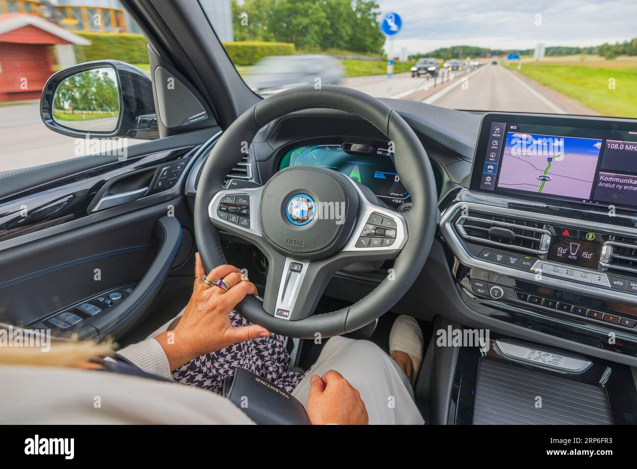 Vue rapprochée de la femme conducteur conduisant la nouvelle BMW iX3 M Sport voiture noire modèle électrique sur l'autoroute. Banque D'Images