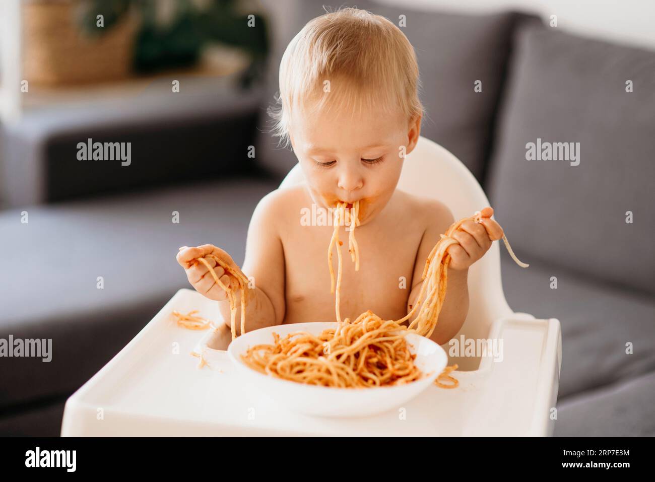 Vue de face bébé garçon jouant avec des pâtes sa chaise haute Banque D'Images