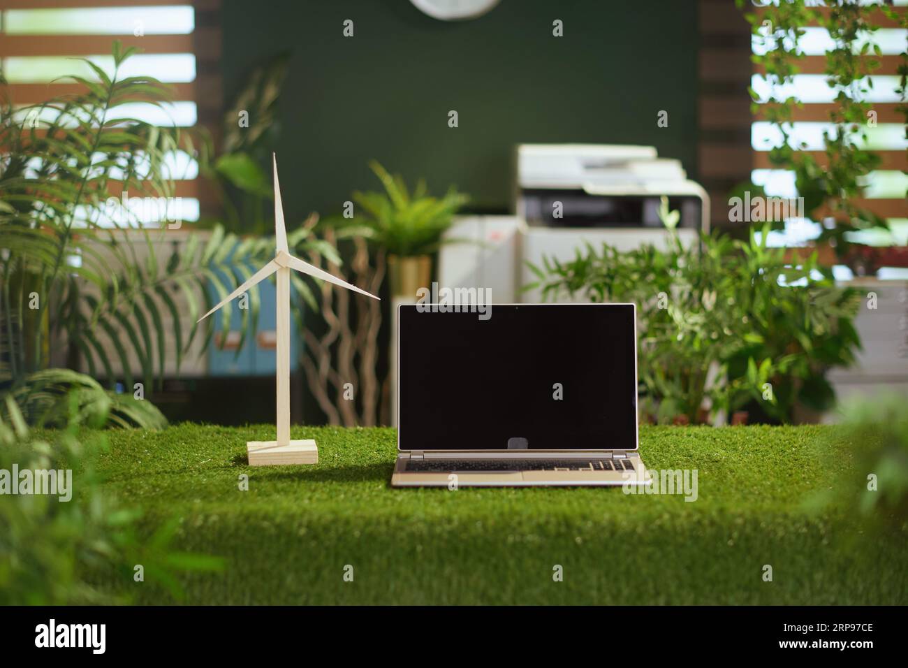 Tendances écologiques. table d'herbe dans le bureau vert moderne avec ordinateur portable, écran vierge et moulin à vent. Banque D'Images