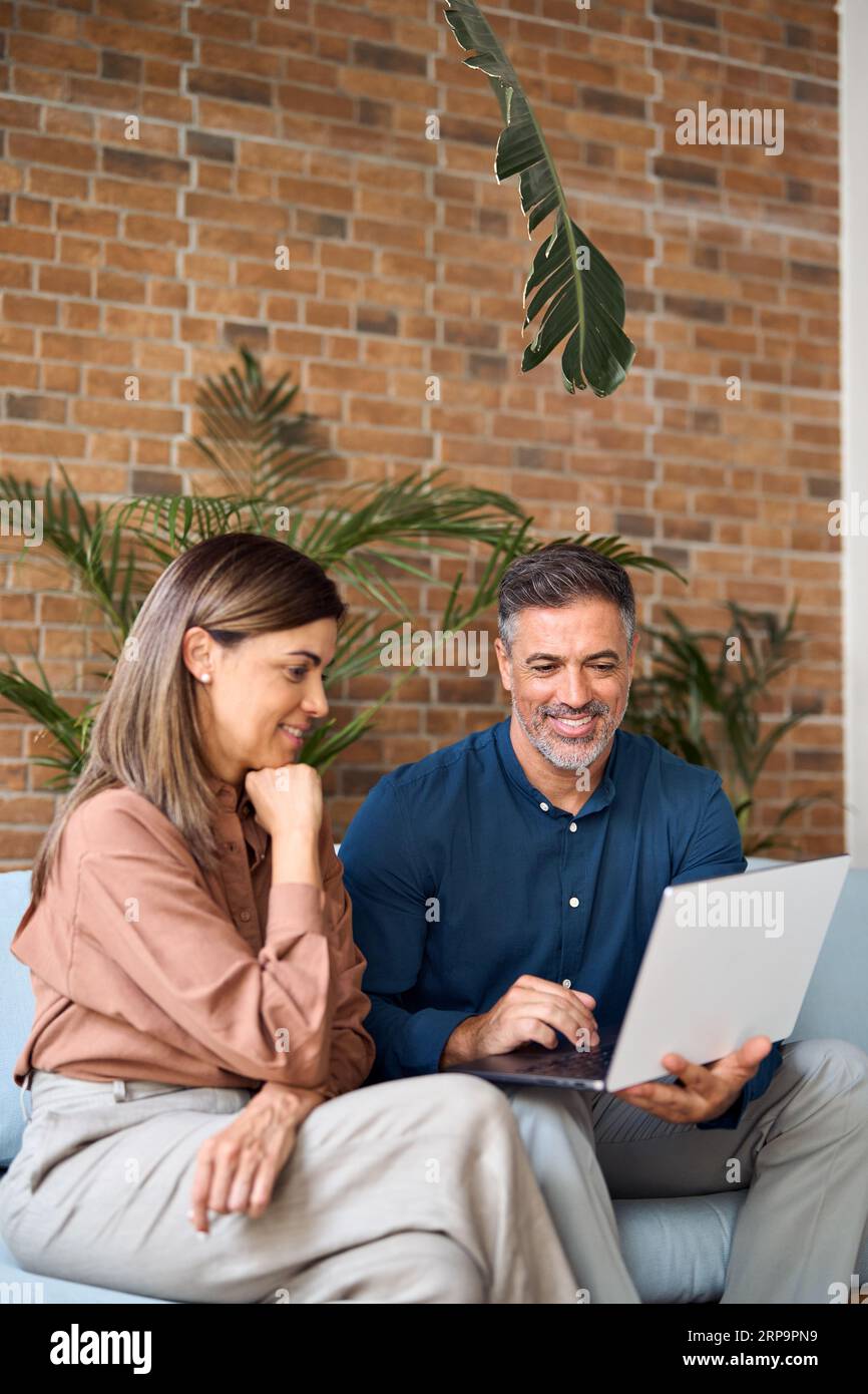 Deux gens d'affaires professionnels heureux parlant à l'aide d'un ordinateur portable dans le bureau. Vertical Banque D'Images