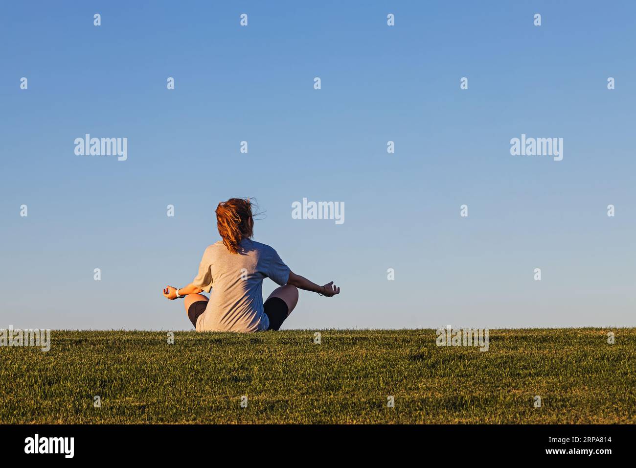 Femme assise dans la pose de lotus sur l'herbe verte au-dessus du ciel bleu, se connectant avec le concept de la nature Banque D'Images