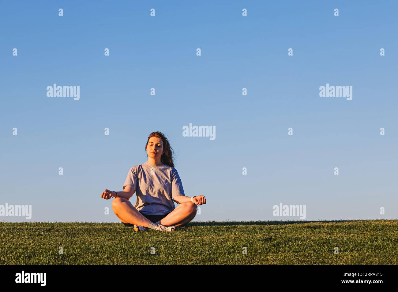 Femme assise dans une pose de méditation sur la pelouse verte au-dessus du ciel bleu, concept de pleine conscience Banque D'Images