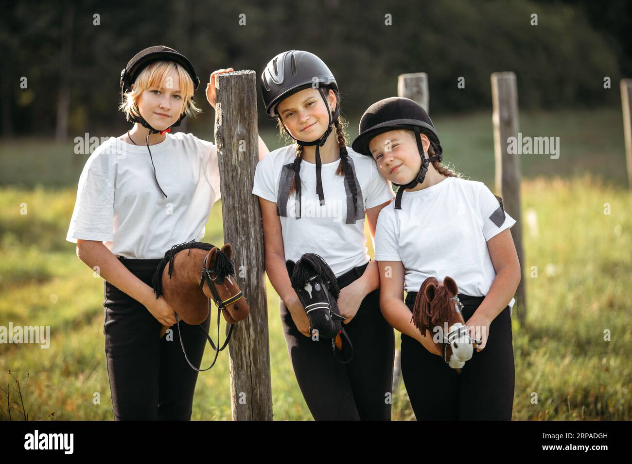 Portrait de filles jockeys assis sur des chevaux jouets près d'un poteau en bois. Banque D'Images