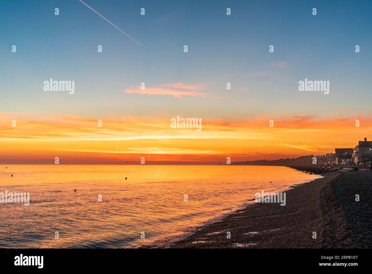 Le ciel de l'aube au-dessus de la plage au bord de la mer à Herne Bay sur la côte nord anglaise du Kent. Un ciel bleu avec une couche vive de nuages rouges et oranges près de l'horizon, l'orange se reflétant dans la mer très calme. Banque D'Images