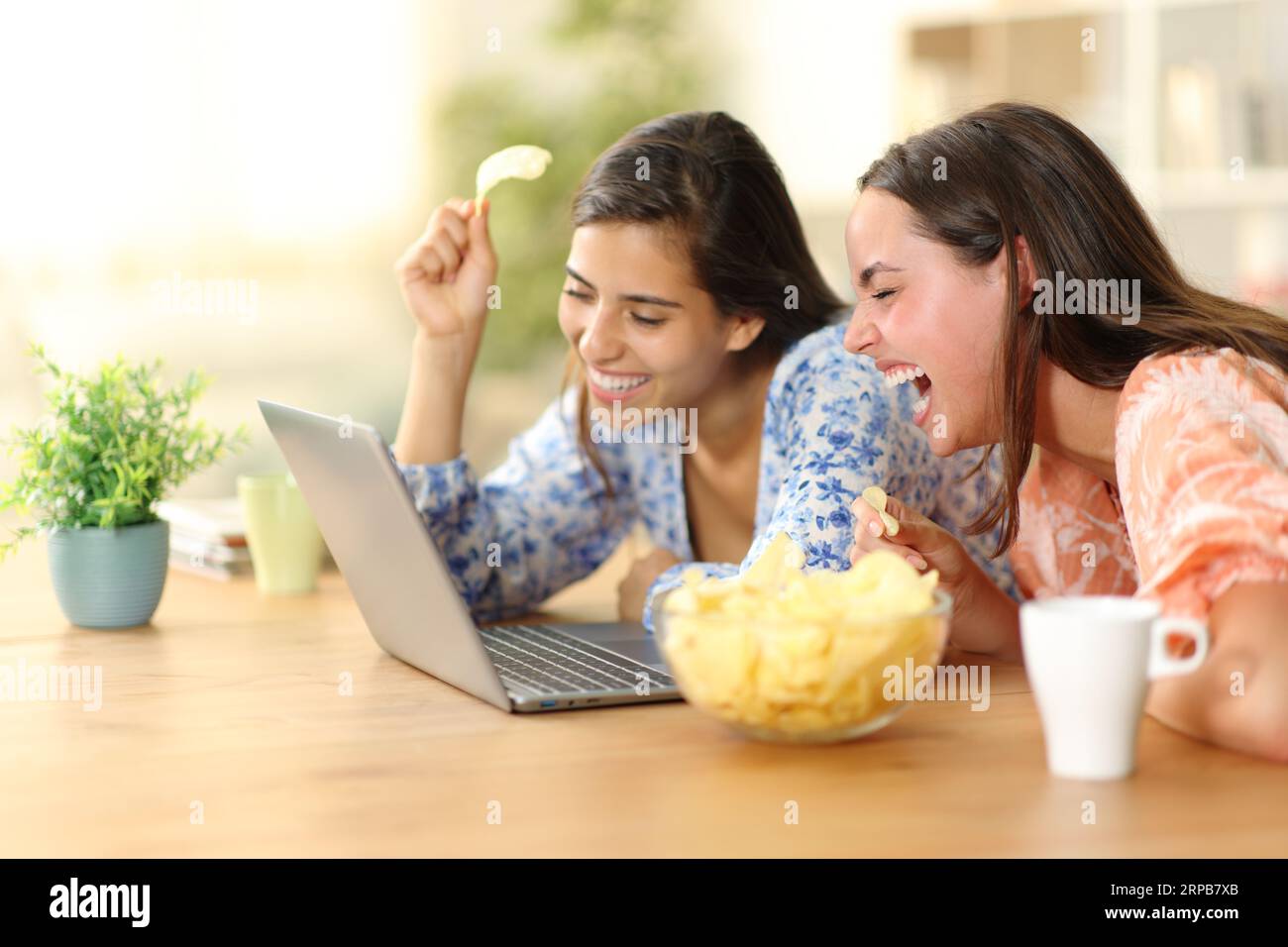 Heureux colocataires riant fort en regardant des vidéos drôles dans un ordinateur portable mangeant des chips à la maison Banque D'Images