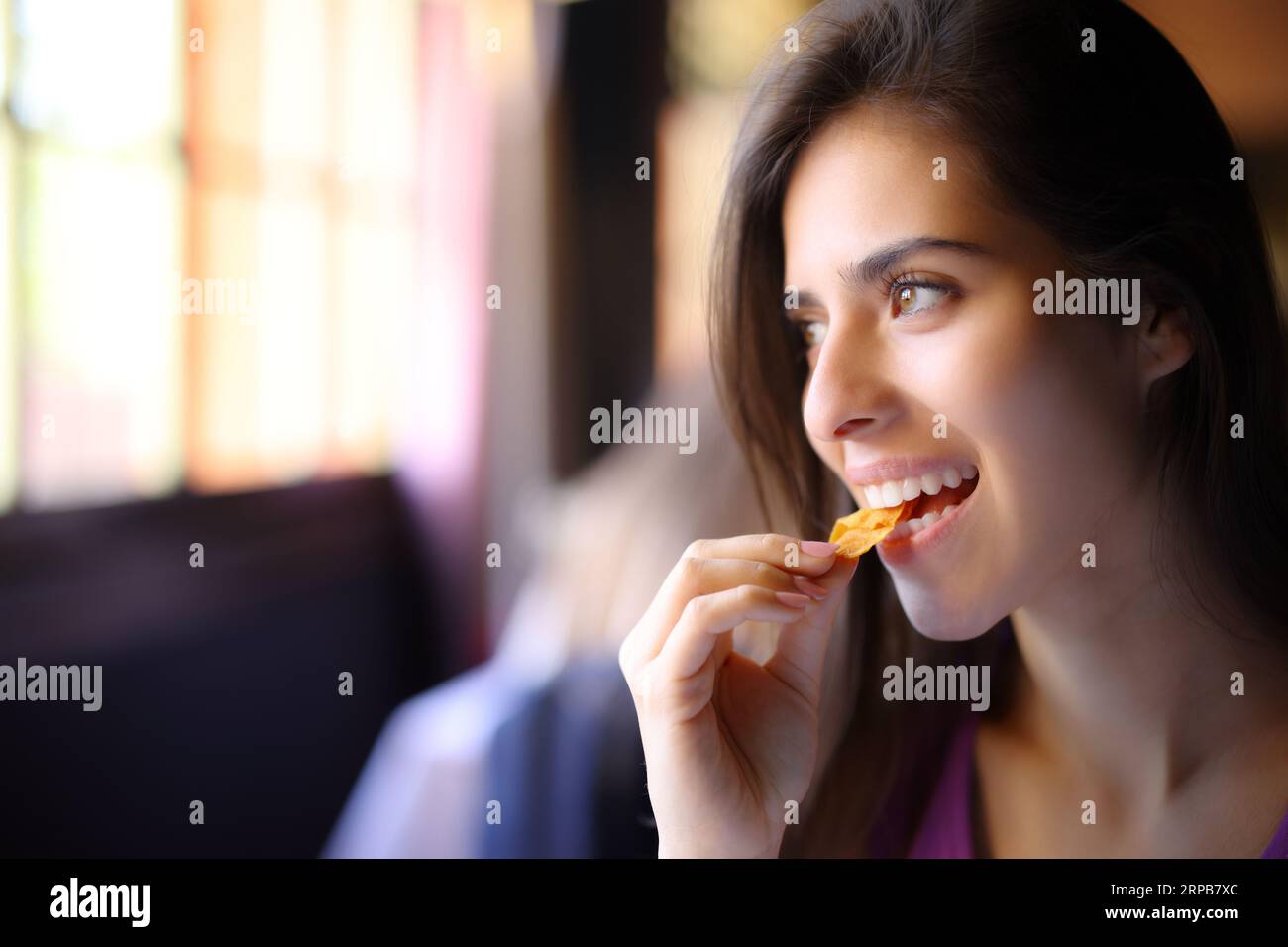 Un client heureux mange des chips et regarde loin par une fenêtre Banque D'Images