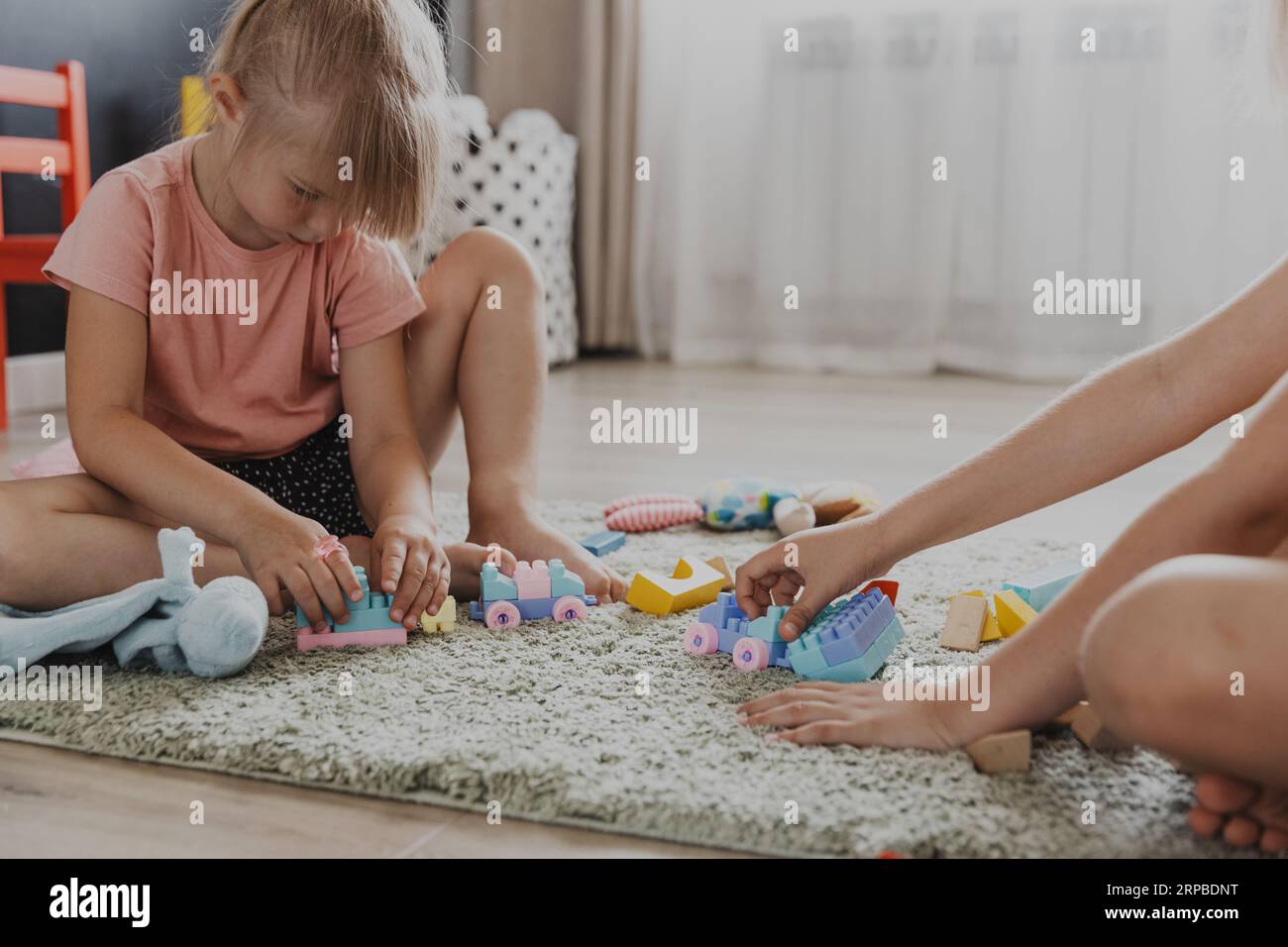Enfants jouant avec le train coloré de jouet en plastique coloré. Les enfants assis sur le tapis à l'intérieur à la chambre à coucher blanche ensoleillée à la maison ou à la maternelle, garderie. Jeu amusant et écologique éducatif pour enfant Banque D'Images