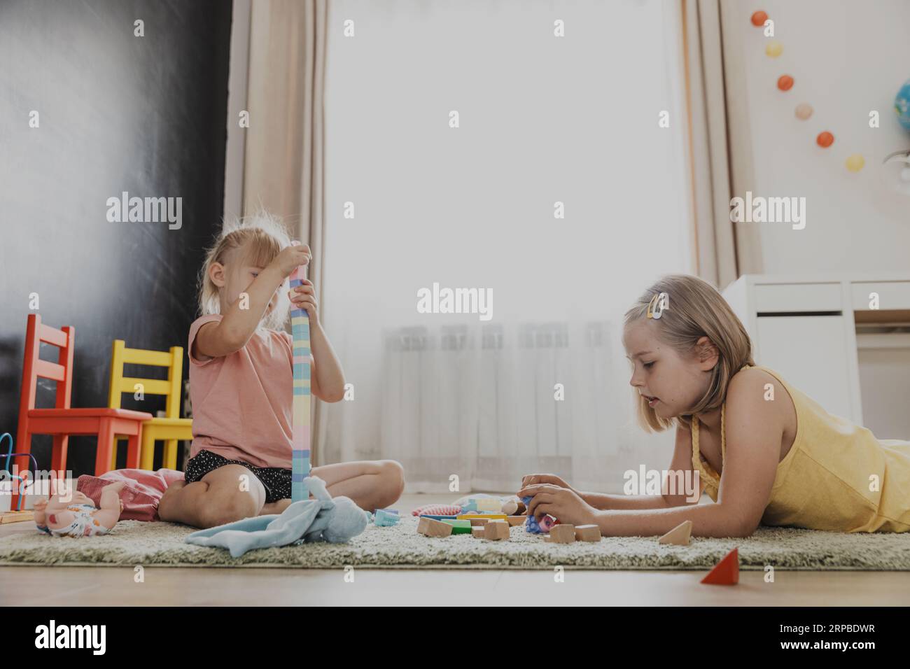 Enfants jouant avec train jouet en bois coloré. Enfants assis sur la moquette à la chambre à coucher à la maison, maternelle, salle de jeux de garderie, aire de jeux, centre de jeux. Jeu amusant et écologique éducatif pour enfant Banque D'Images
