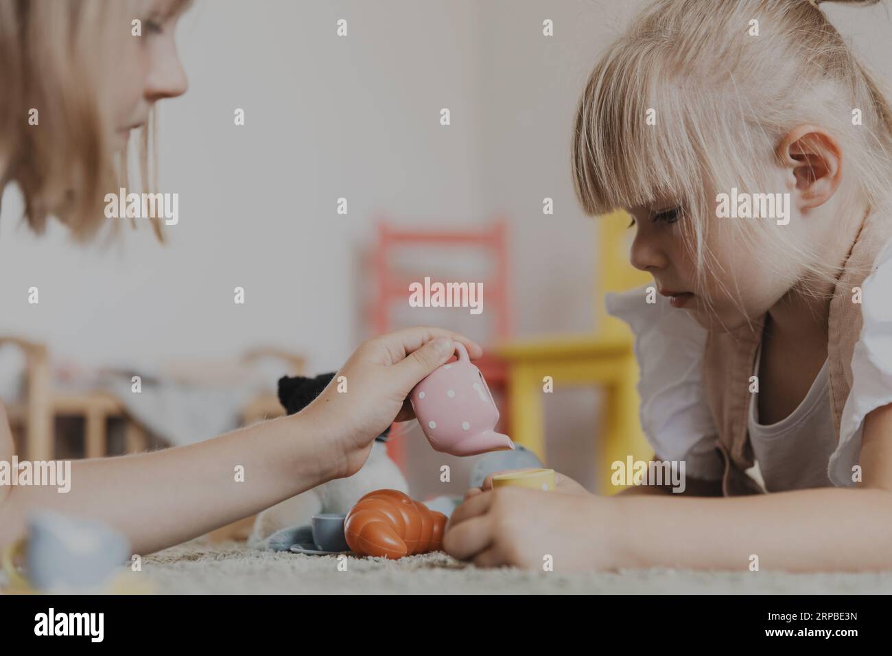 Gros plan d'enfants féminins jouant avec un ensemble de thé de jeu de cuisine coloré. Enfants couchés sur tapis dans la chambre à la maison, jardin d'enfants. Jeux écologiques éducatifs. Développement de la motricité, imagination Banque D'Images