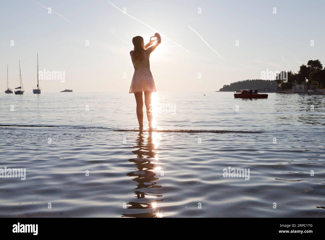 Une adolescente encadre une photo du coucher de soleil sur le lac Banque D'Images