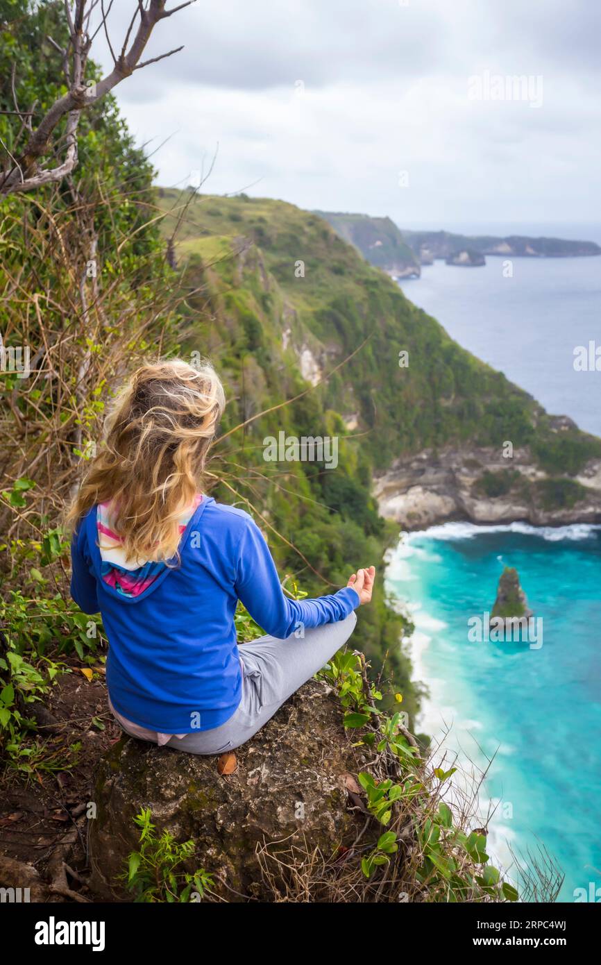 Femme blonde méditant sur le bord de la falaise côtière, Bali, Indonésie Banque D'Images