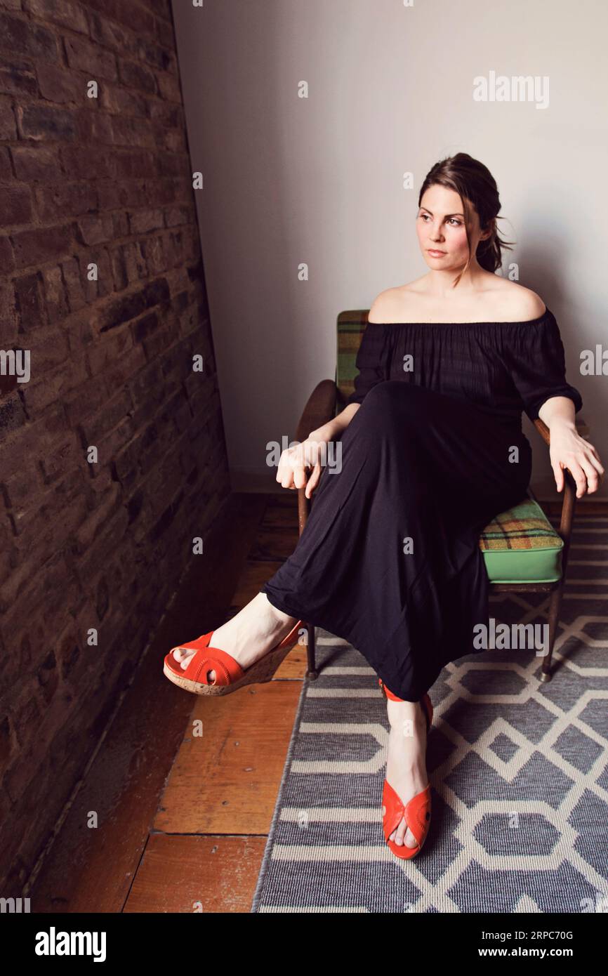 Une femme dans un haut de lierre est assise dans une chaise tout en regardant par une fenêtre Banque D'Images