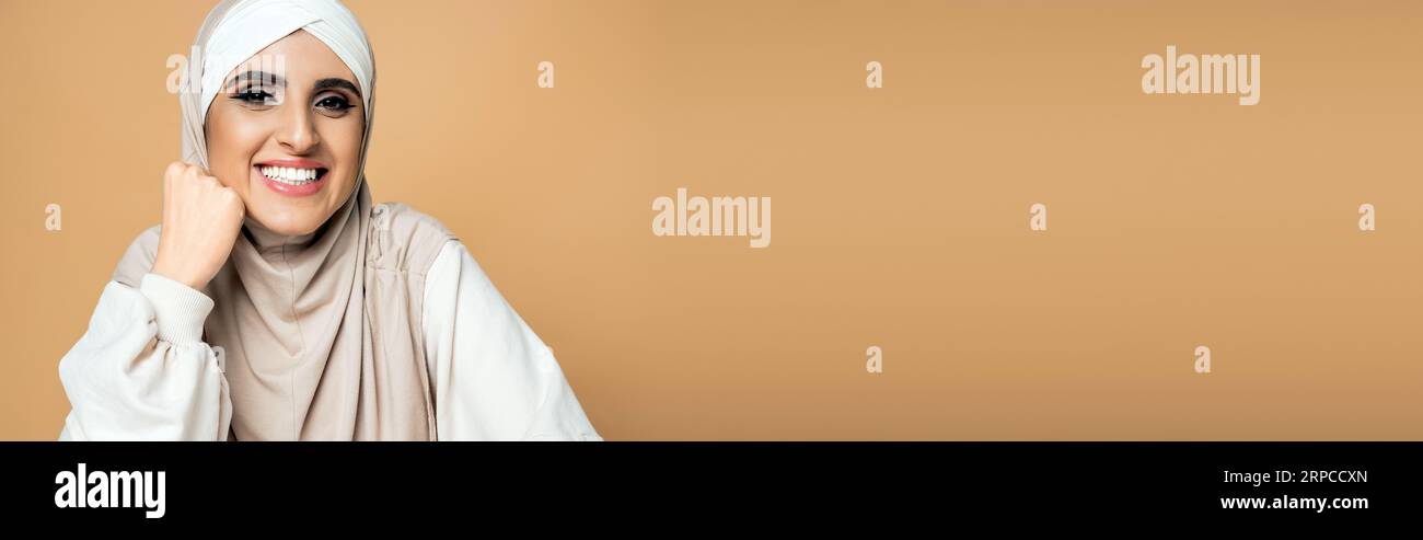 joyeuse femme musulmane en sweat-shirt blanc et hijab regardant la caméra sur beige, style personnel, bannière Banque D'Images