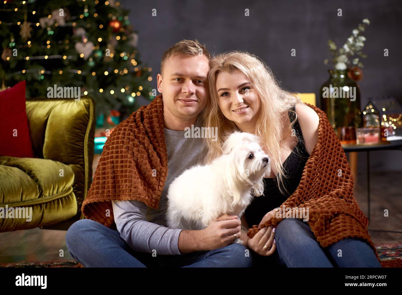 Charmant couple romantique avec leur chien près de l'arbre de Noël dans l'intérieur de maison confortable esthétique festive. Franc, vrai moment. Bonne humeur et avoir du plaisir à faire Banque D'Images