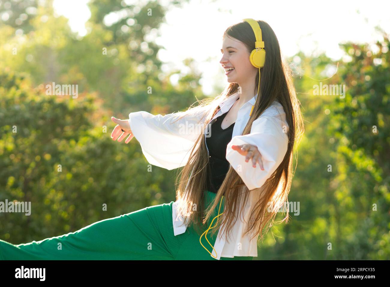 Adolescente aux cheveux longs écoute de la musique dans des écouteurs jaunes et danse dans le parc en été journée ensoleillée. Adolescent aime la vie insouciante et la liberté en plein air Banque D'Images