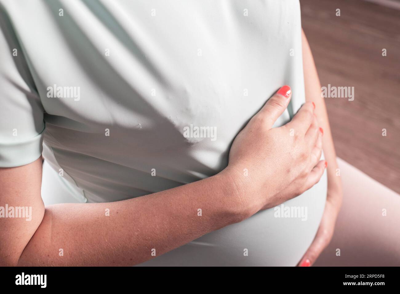 Une fille enceinte tient son estomac dans la zone du plexus solaire. Le concept de douleur chez la femme enceinte due à la pancréatite, à une mauvaise posture et au stress. Banque D'Images