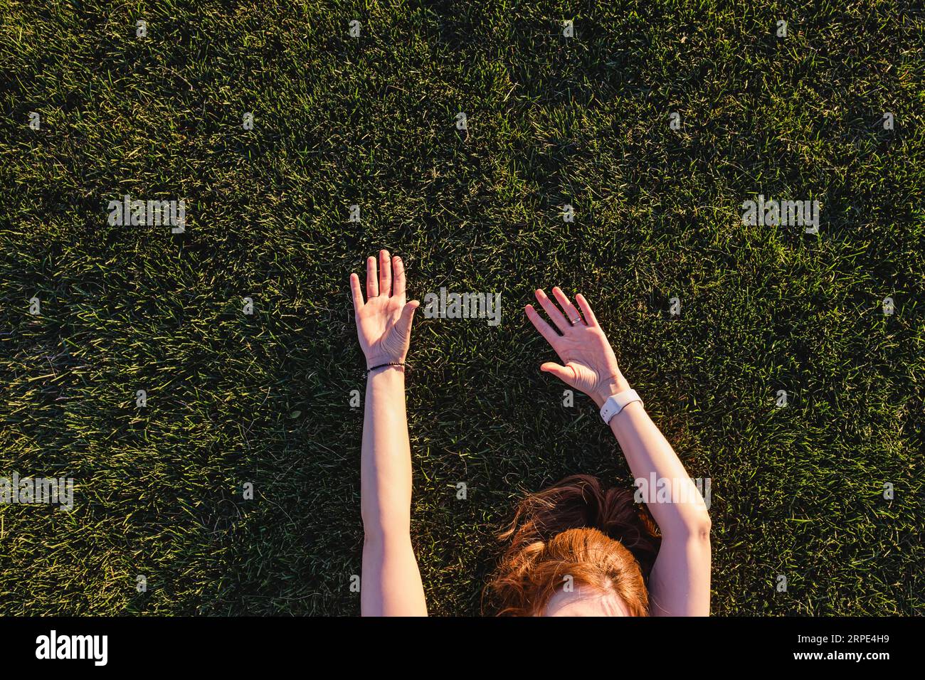Femme méconnaissable couchée sur l'herbe verte avec ses mains levées, vue depuis le haut Banque D'Images