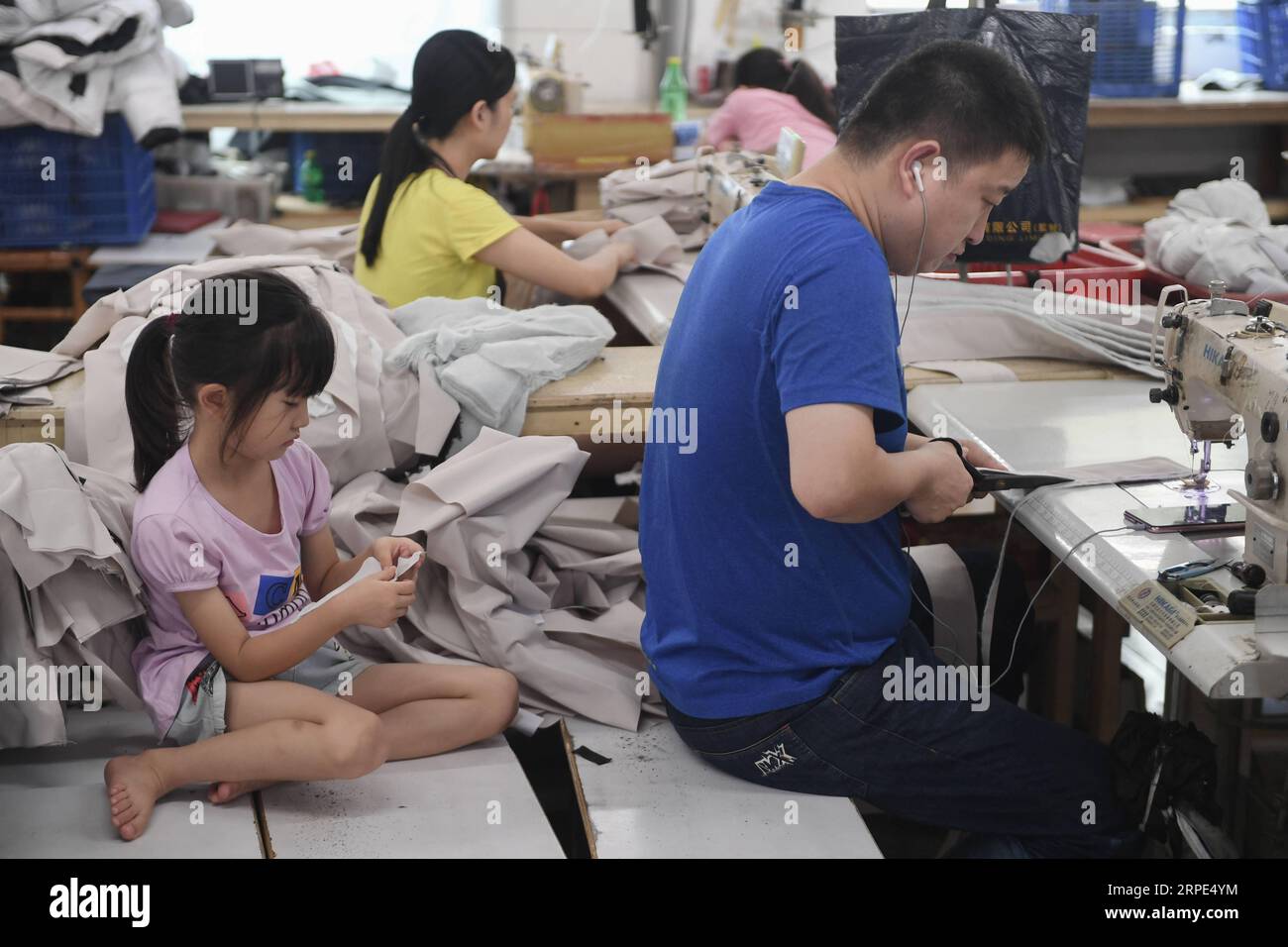 (190818) -- BEIJING, 18 août 2019 -- Wang Jingjing (à gauche) s'assoit à côté de son père dans l'atelier d'une usine de vêtements à Shishi, dans la province du Fujian du sud-est de la Chine, le 2 août 2019. La chaleur brûlante a englouti Shishi du Fujian du sud-est de la Chine cet été, laissant peu de gens marcher dans les rues habituellement animées. En revanche, les usines de vêtements, qui sont densément disséminées dans la ville, sont bondées de gens qui ont été submergés par leur travail car l'été est la haute saison pour la confection de vêtements chaque année, ainsi que leurs enfants. Le statut réputé de Shishi en tant que vêtement majeur Banque D'Images