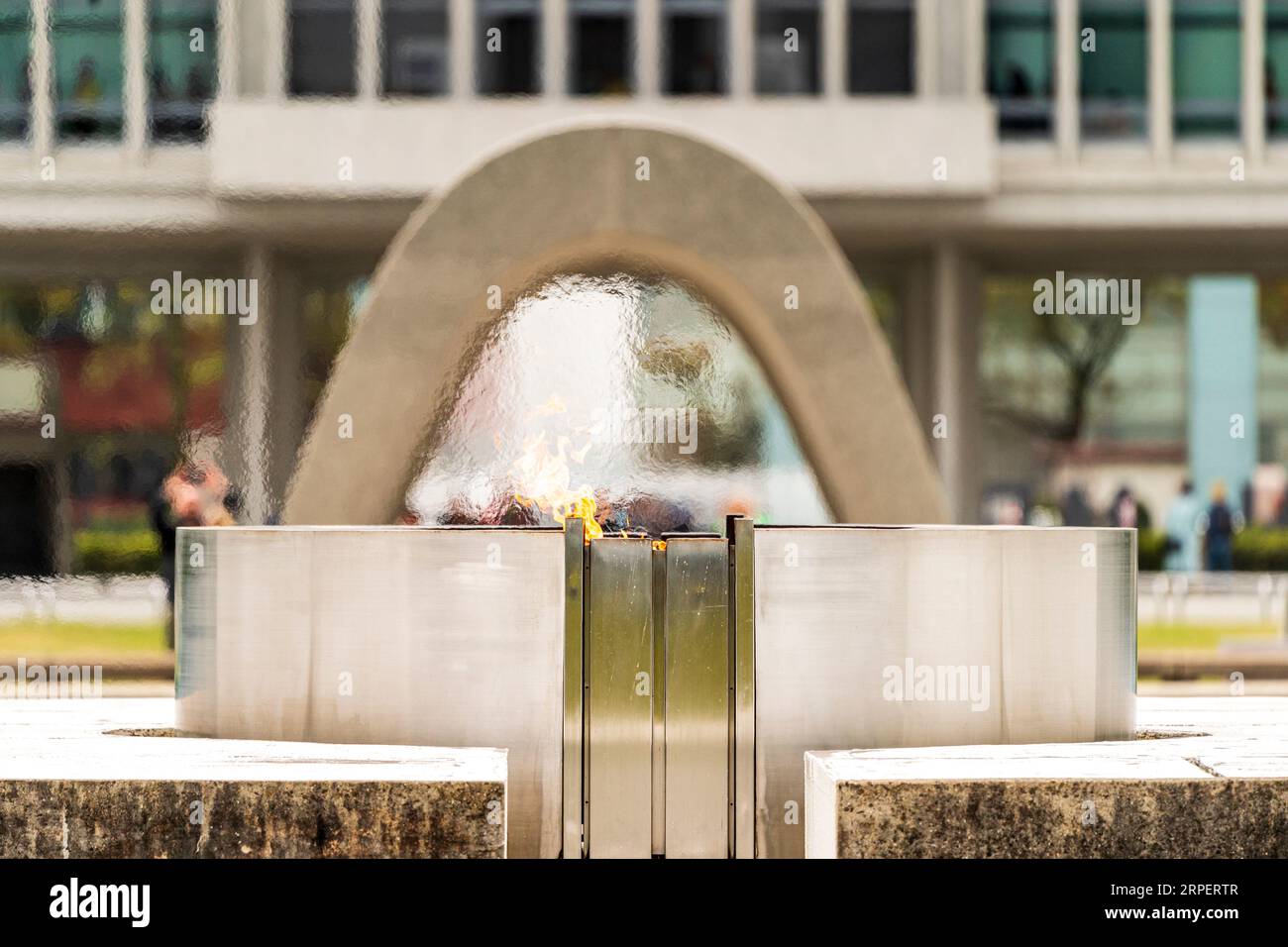 La flamme de la paix, conçue par Kenzo Tange, au parc commémoratif de la paix d'Hiroshima avec le monument en forme de selle qui recouvre un cénotaphe derrière. Banque D'Images