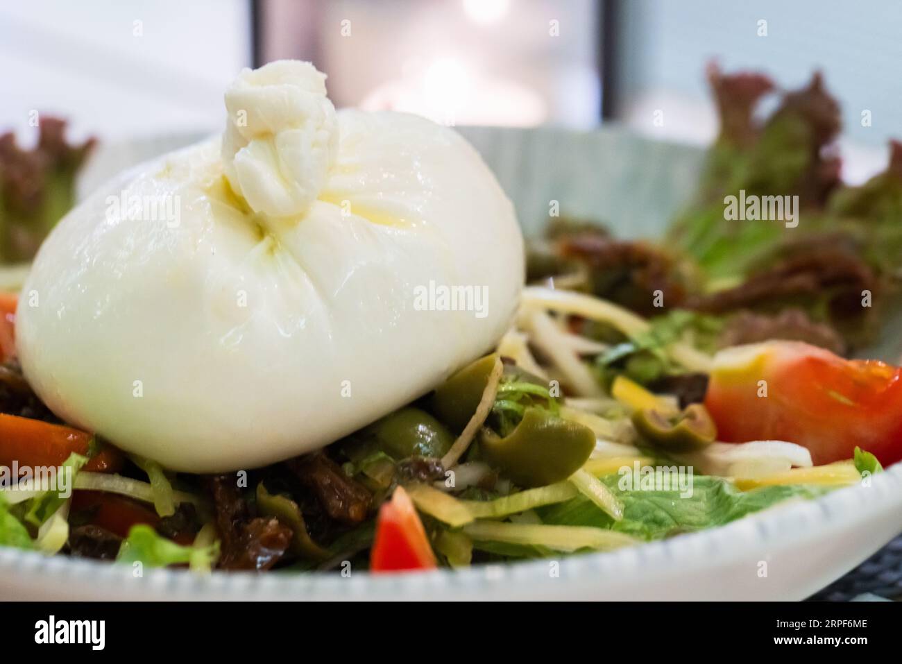 La burrata est sur une assiette avec des légumes. Il s'agit d'un fromage italien au lait de vache ou de buffle à base de mozzarella et de crème Banque D'Images