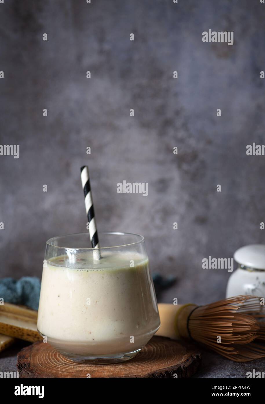 Smoothie frais et sain à la banane et à la poire, dans une tasse en verre avec un tube noir-blanc, sur un plateau en bois et un fond gris Banque D'Images