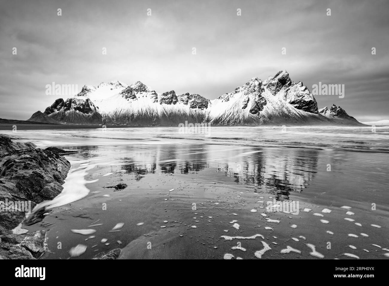 Image en noir et blanc d'une formation de montagne couverte de neige reflétée dans l'eau d'une plage de sable de lave noire, grand effet de profondeur - lieu : Islande, Banque D'Images