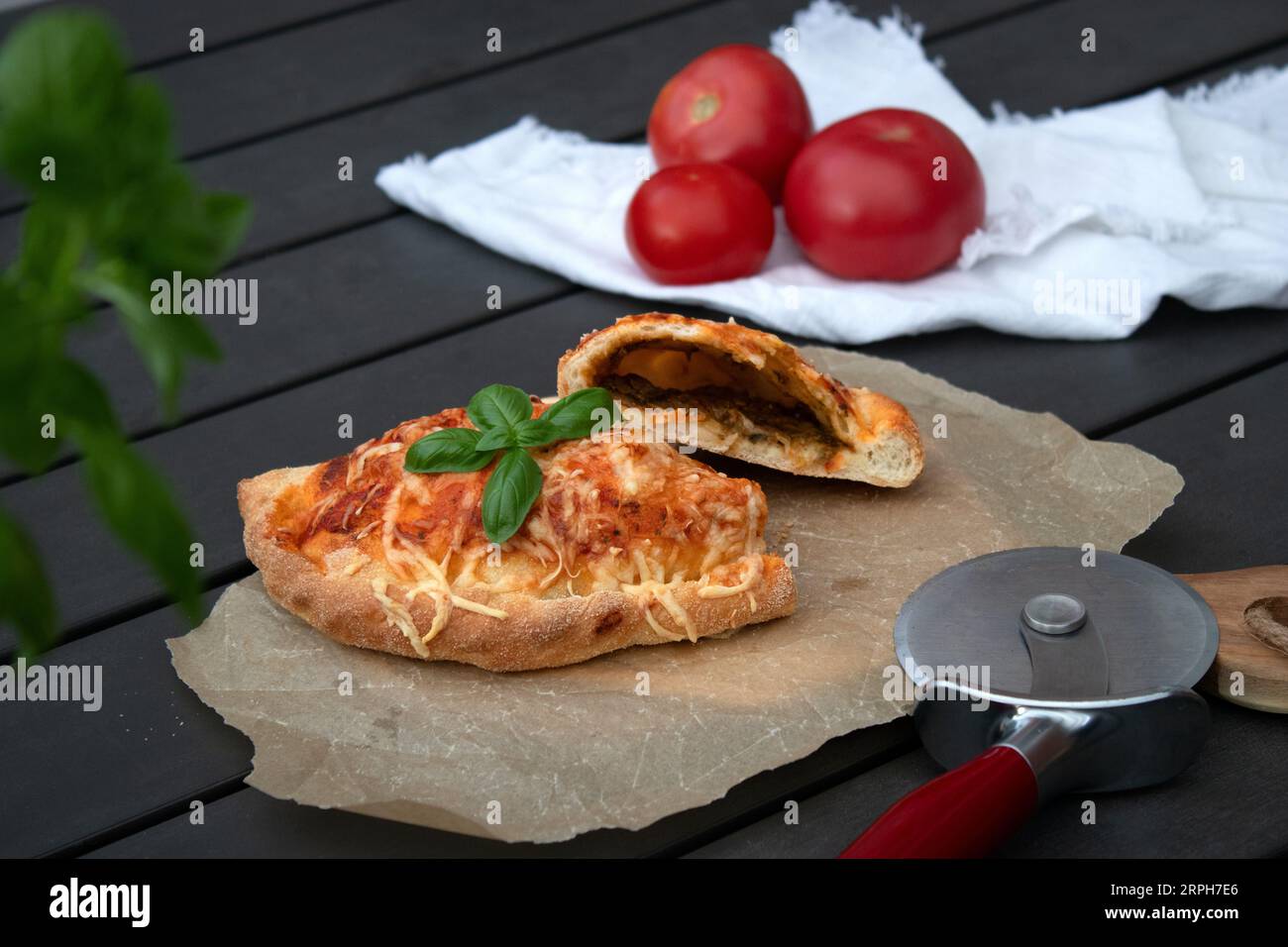Pizza calzone découpée avec sauce tomate, pesto vert et fromage sur assiette en bois Banque D'Images