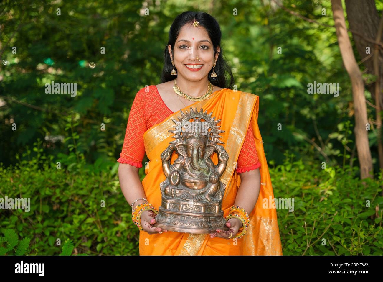 Heureuse jeune femme indienne portant Saree tenant lord Ganesha idole en plein air au parc célébrant le festival Ganesh Chaturthi. Banque D'Images