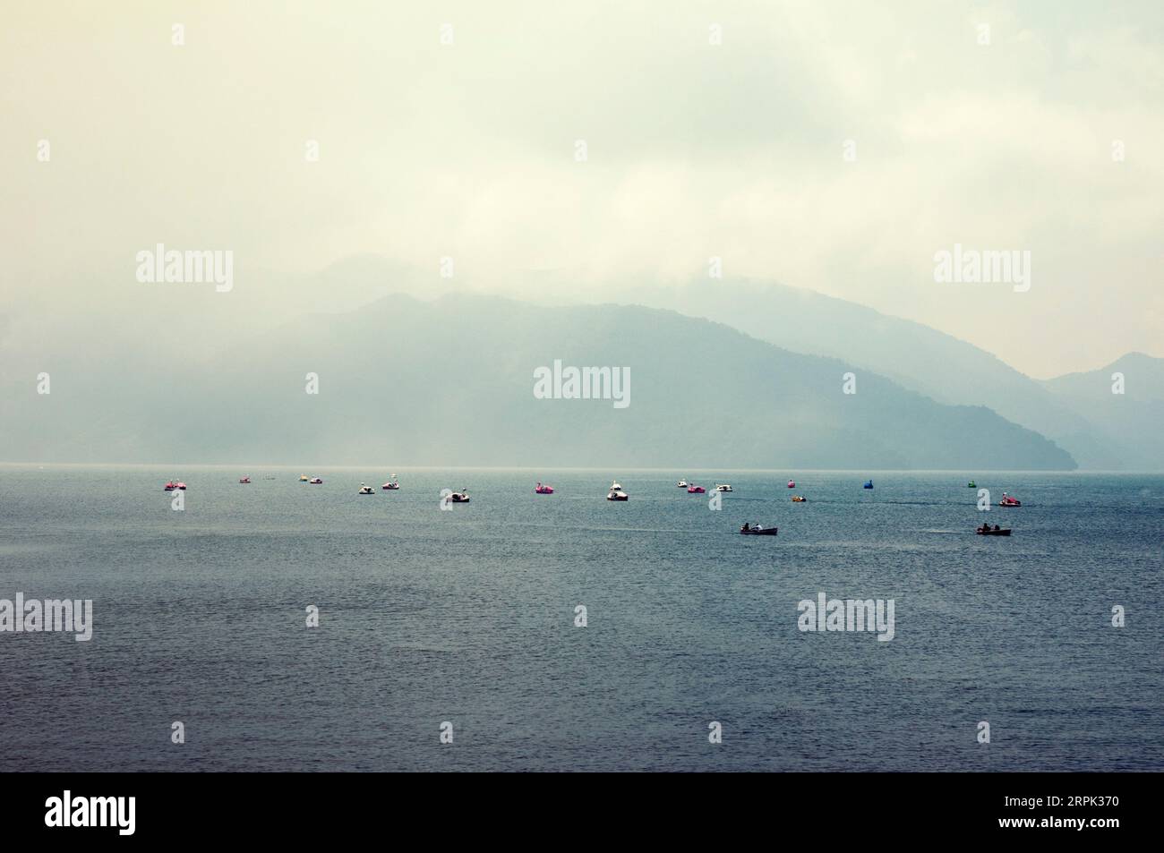 Atmosphère humide nuageuse sur le lac de montagne plein de bateaux touristiques, c'est le célèbre lac Chuzenji au Japon. Banque D'Images