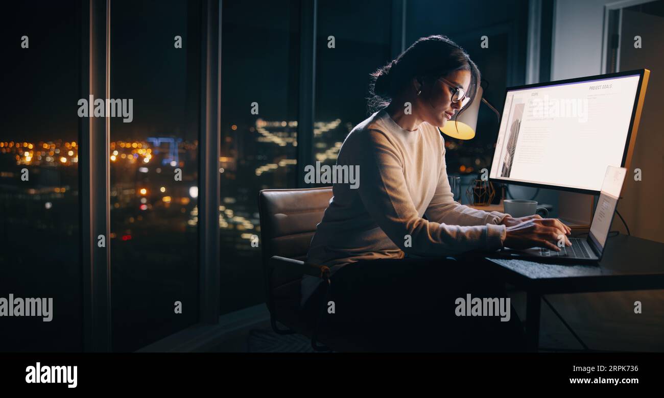 Femme d'affaires caucasienne travaillant tard à son bureau, tapant sur son ordinateur portable dans un bureau axé sur la technologie. Jeune professionnelle féminine se concentrant sur son projet Banque D'Images