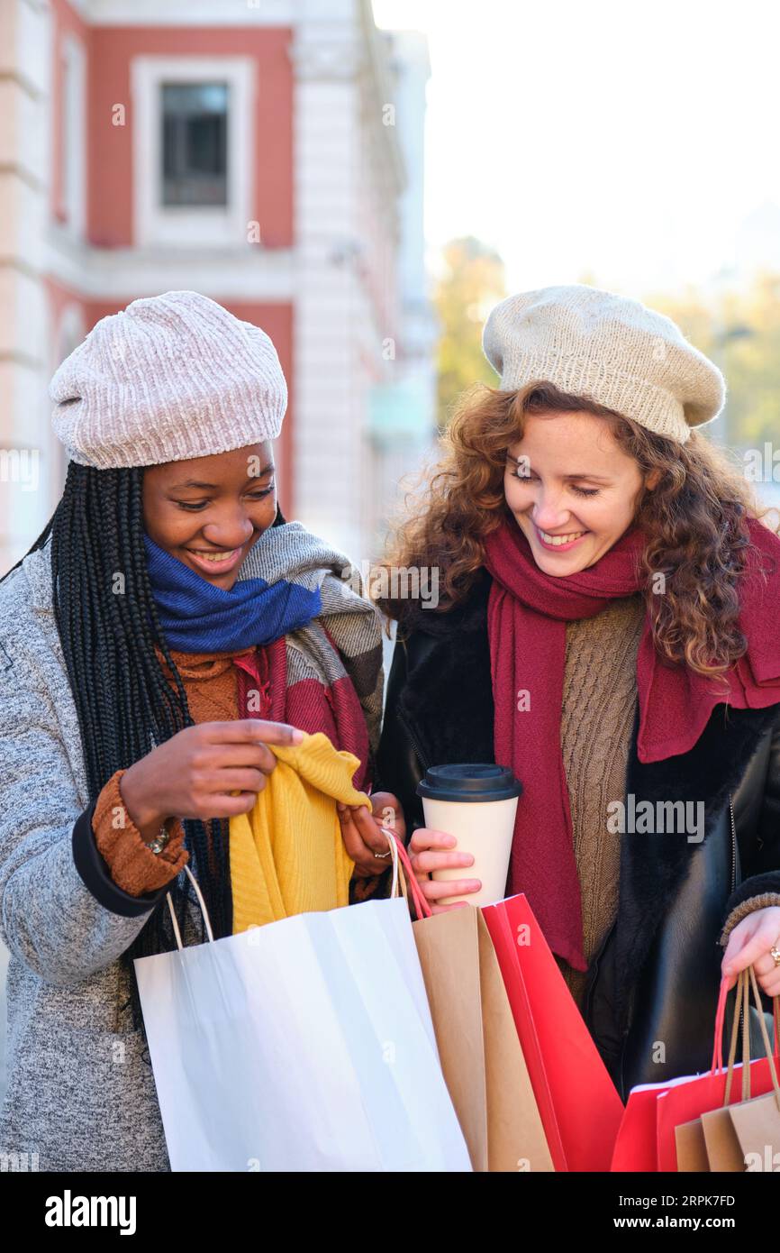 Deux amies multiraciales à la recherche des vêtements qu'elles ont achetés après avoir fait du shopping en hiver. Banque D'Images